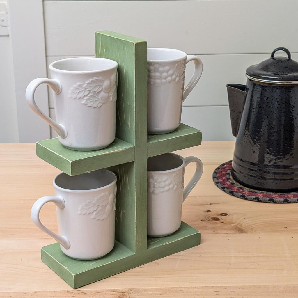 DIY stacked mug stand painted green with a distressed finish, holding four white mugs on a wood counter beside a black coffee pot