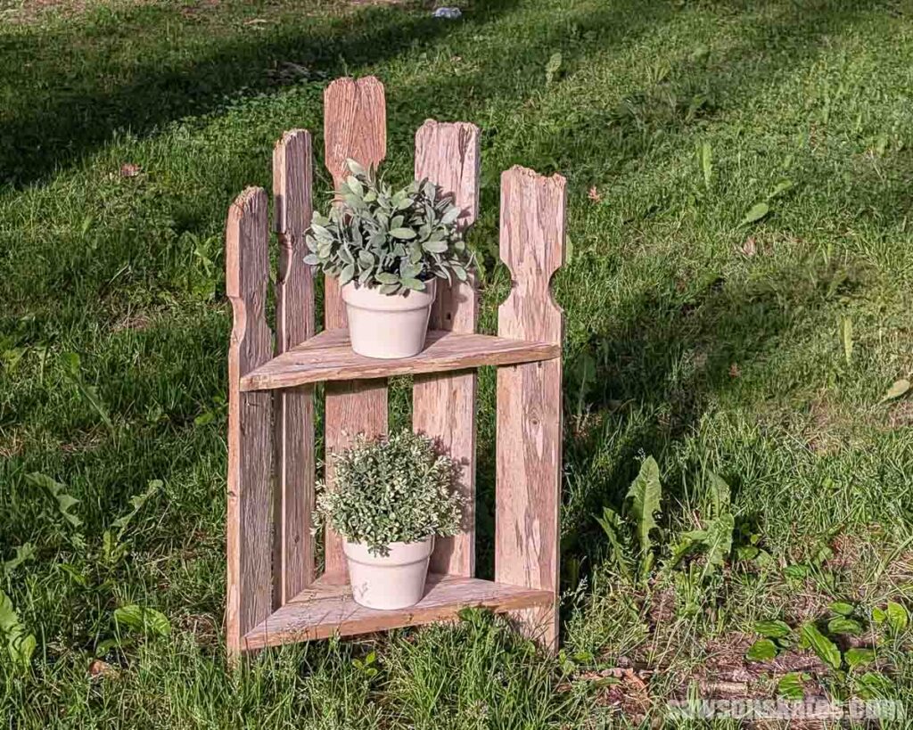 A two-tier plant stand with plants in a yard.