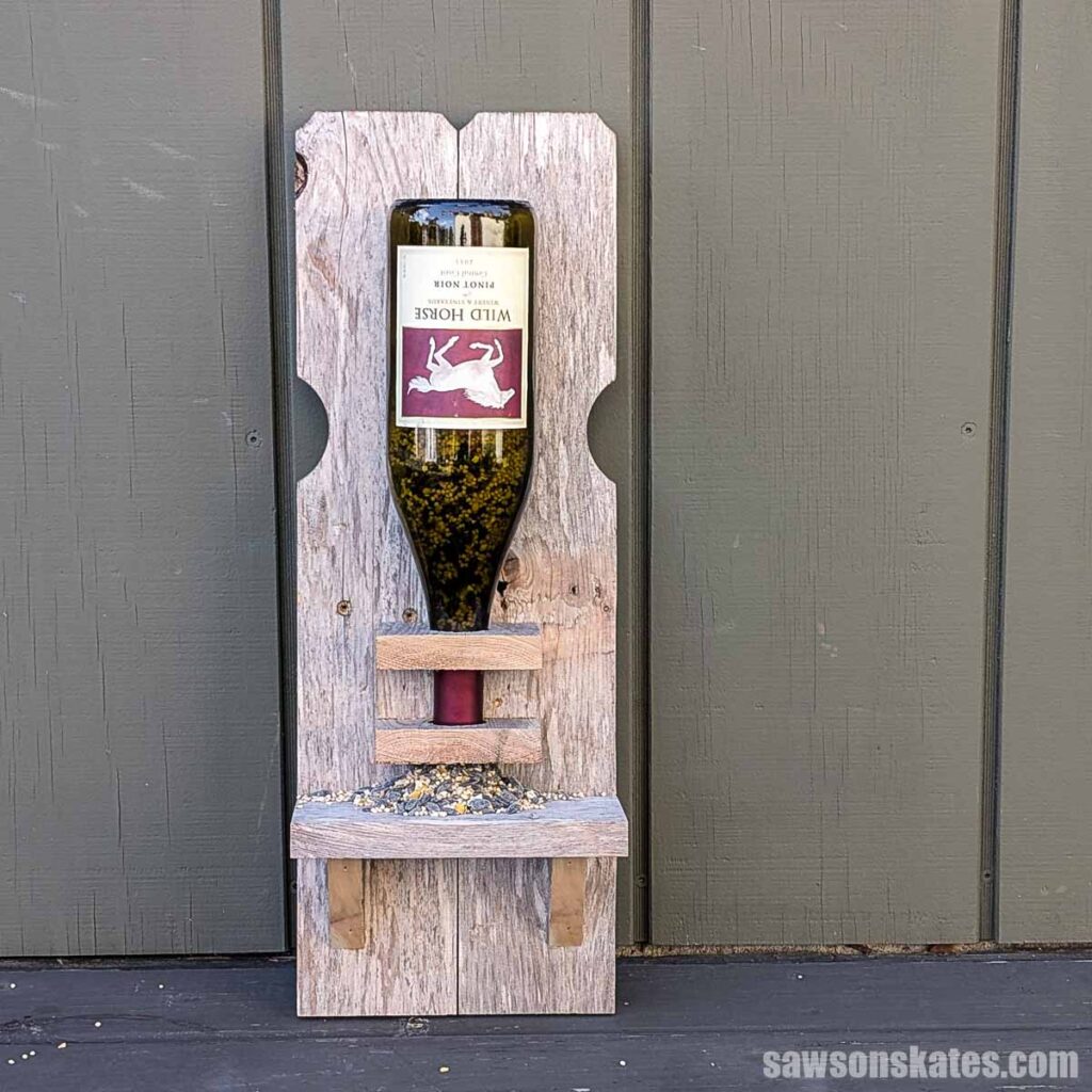 Front view of a wooden bird feeder made from reclaimed fence pickets and a wine bottle