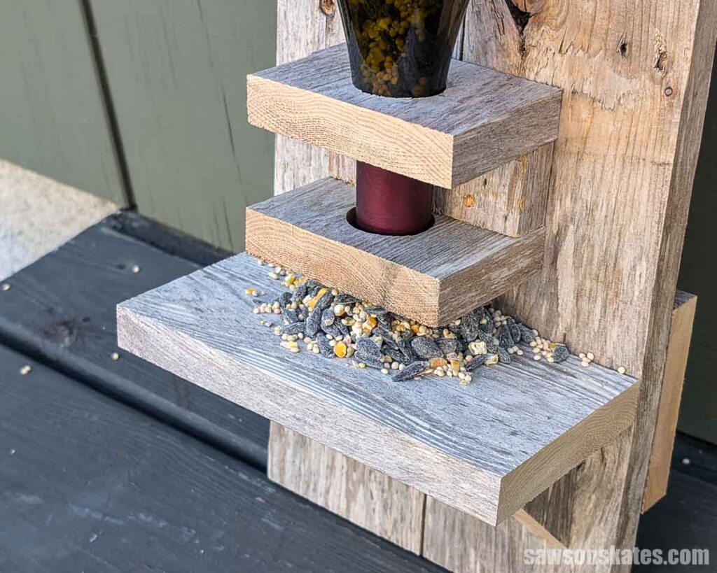 Close up of birdseed in a wooden bird feeder made from reclaimed fence pickets and a wine bottle