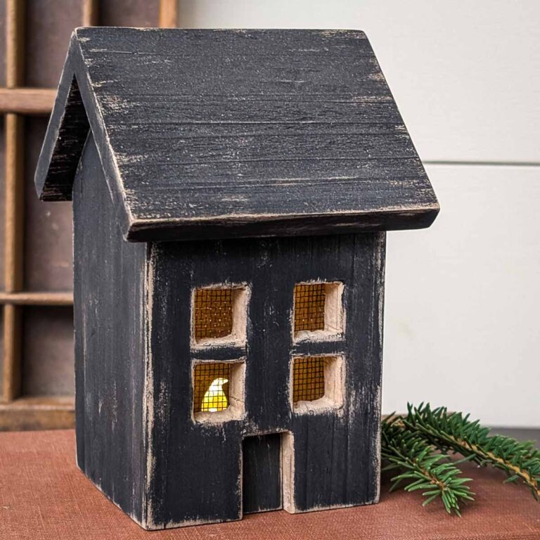 DIY wood house luminary with an LED candle inside sitting on a book with a sprig of evergreen on the right side