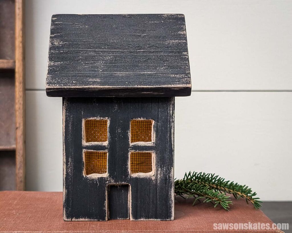 Front view a of wood house luminary with an evergreen spring sitting on a book