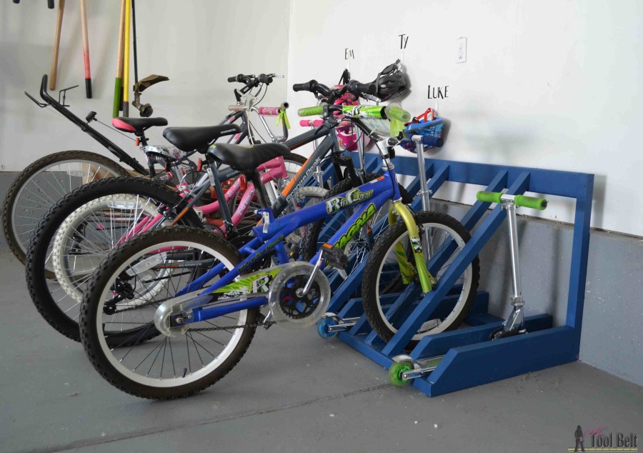 Kids’ bikes and scooters parked in a blue wooden garage bike rack.