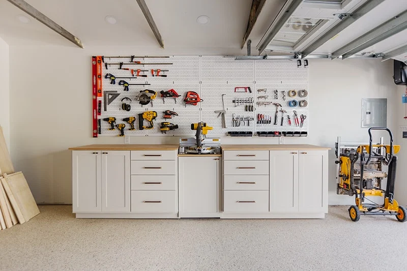 Garage workshop wall with cabinets, a workbench, pegboard tool storage, and a miter saw station.