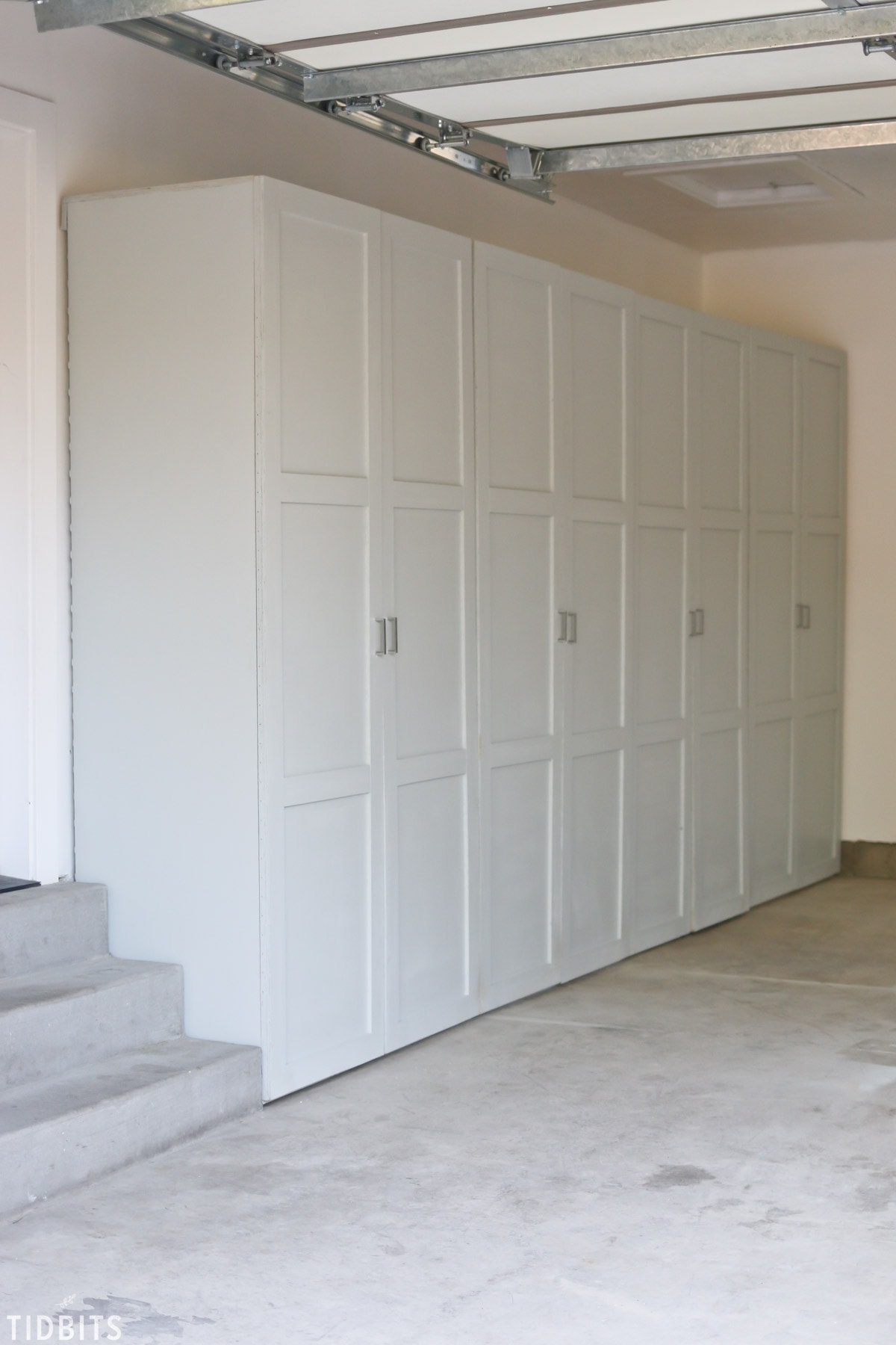 Floor-to-ceiling garage storage cabinets with paneled doors installed along one wall near the garage stairs.