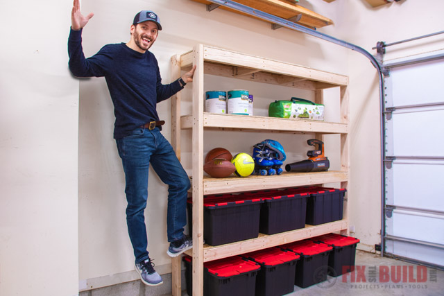 Person standing beside a wooden garage storage shelf with sports gear, paint cans, and plastic storage bins.