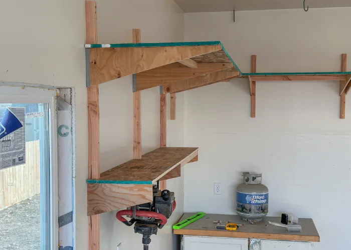 Wall-mounted garage shelves with plywood supports and wood framing.