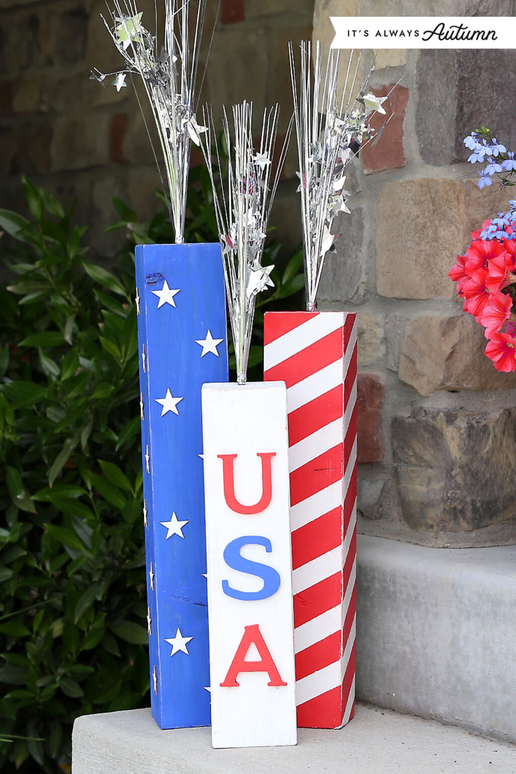 Patriotic porch decoration made from three tall wooden blocks painted in red, white, and blue.