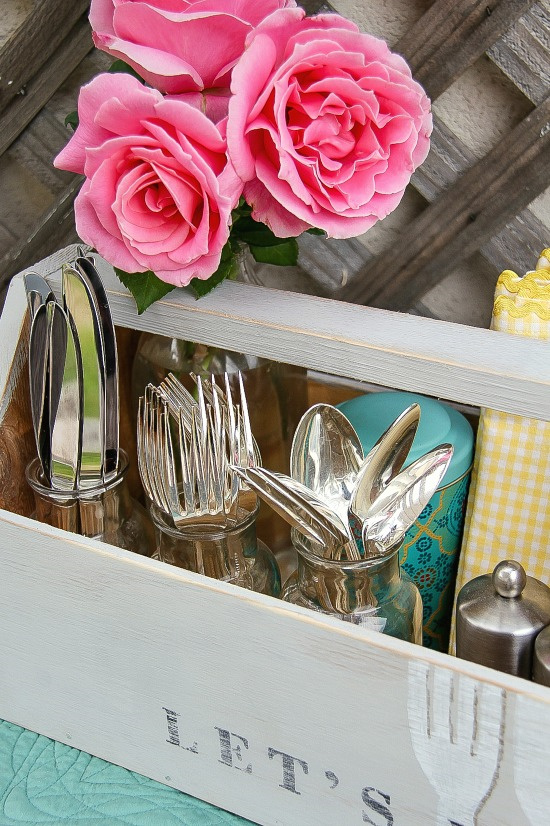 Wooden picnic caddy holding silverware, napkins, salt and pepper shakers, and table decor.