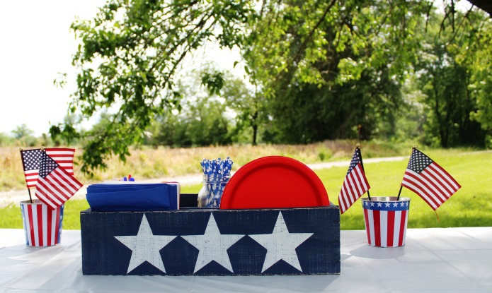Patriotic tabletop organizer painted dark blue with three large white stars across the front. The wooden caddy holds red plates, blue napkins,