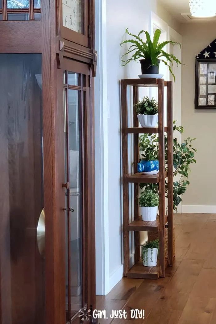 Wooden plant stand tower stained dark next to a wall
