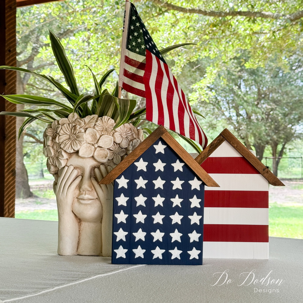 Two small wooden house-shaped decorations painted with an American flag theme sit on a white tabletop.