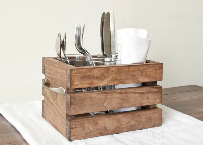 Rustic wooden utensil caddy holding forks, knives, spoons, and napkins on a table.