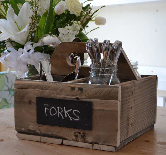 Wooden utensil caddy with a chalkboard label for forks holding mason jars of flatware.