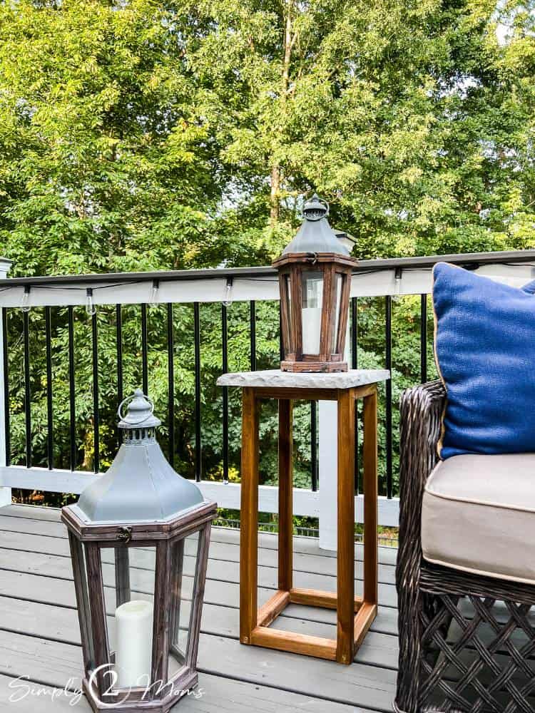 Tall outdoor side table with a concrete top and slim wood base stands beside a wicker patio chair on a deck.