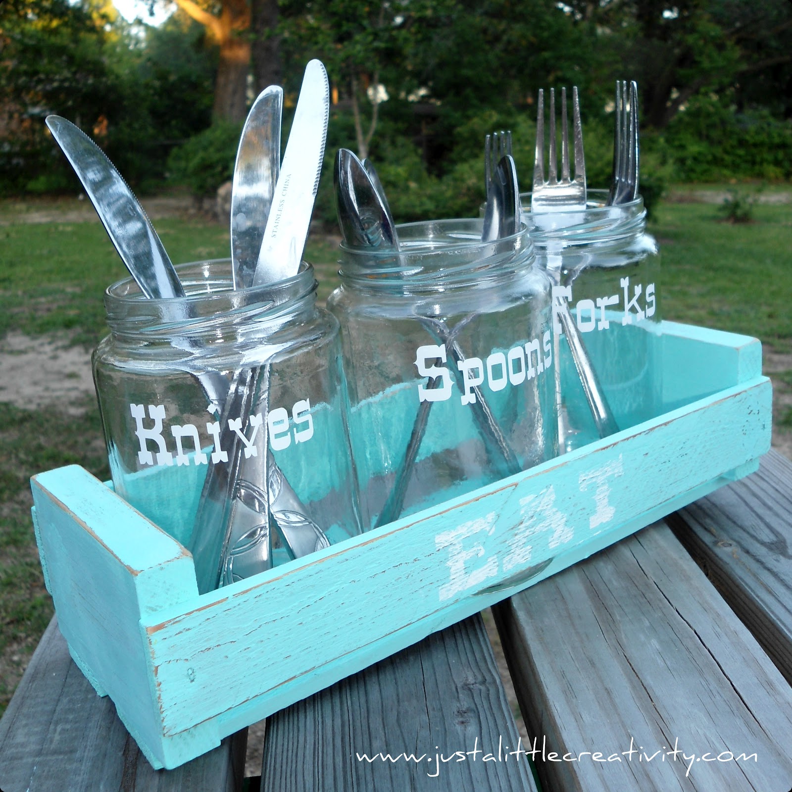 Turquoise wooden utensil caddy holding mason jars labeled for knives, spoons, and forks.