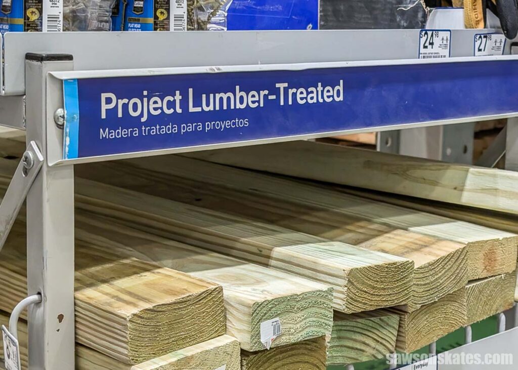 Display at a home improvement store that says Project Lumber-Treated with a pile of pressure treated wood on the shelf